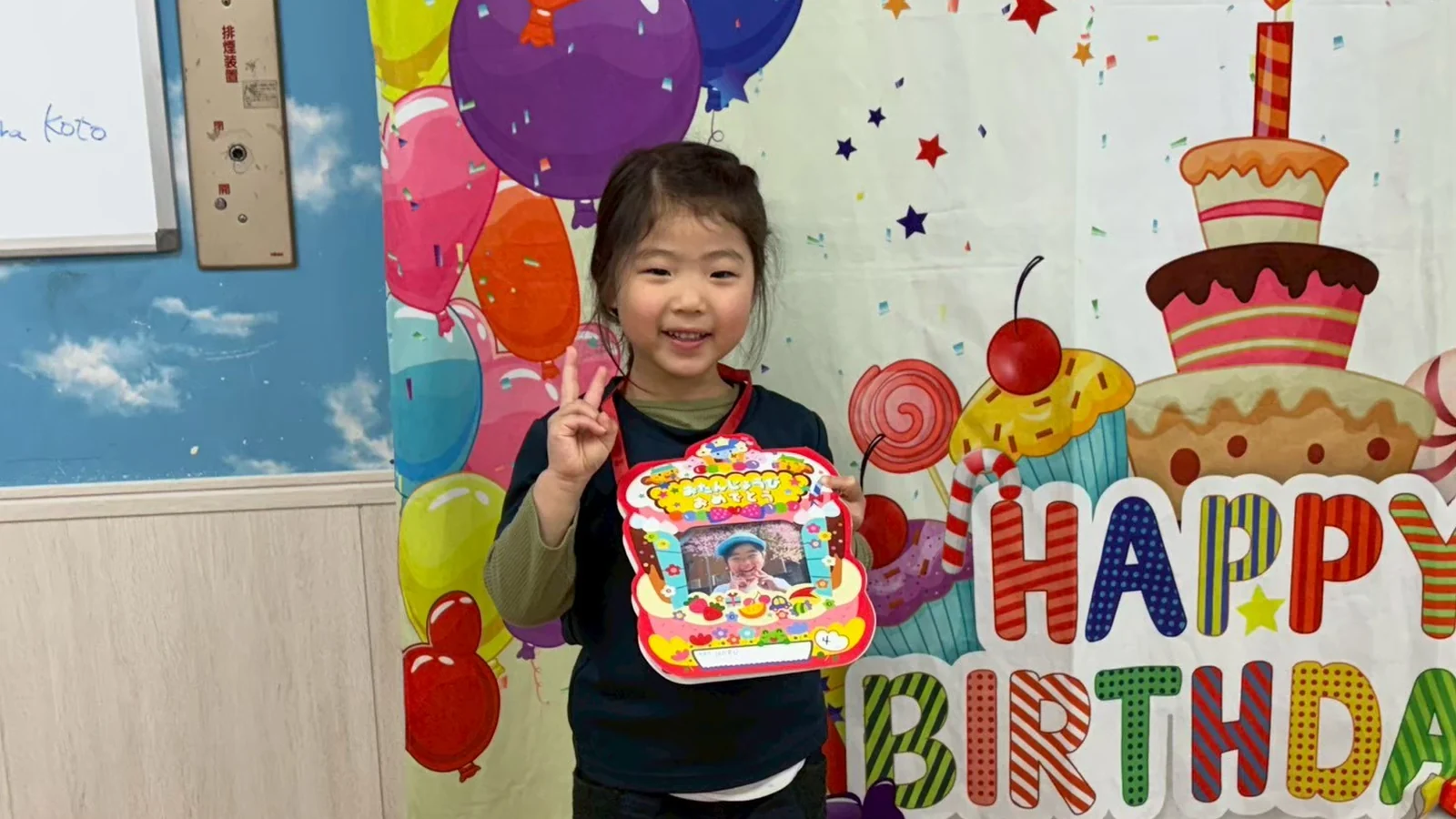 誕生日の飾りの前でカードを持つ子ども